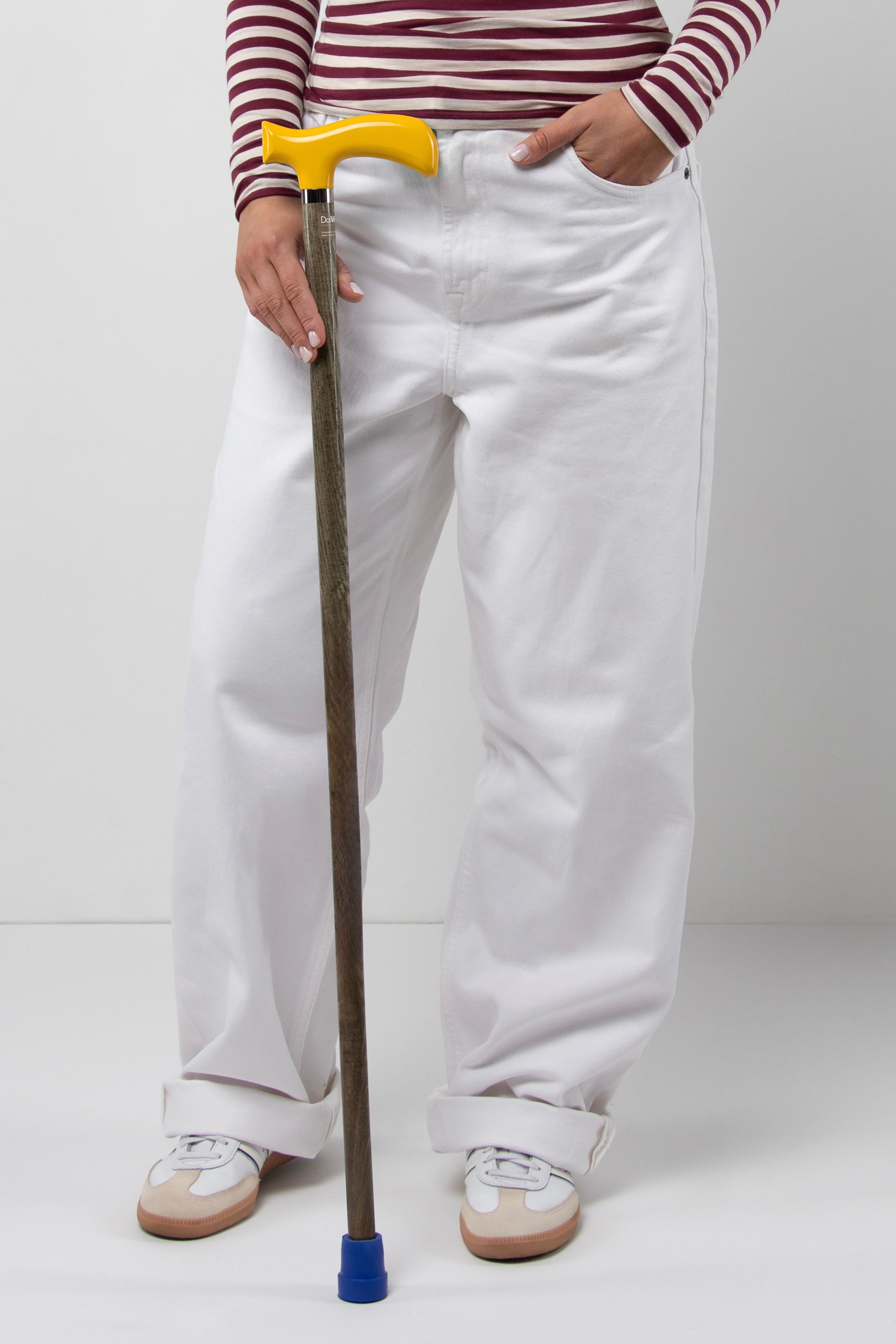 Bright young woman's walking cane with traffic yellow handle on light natural oak wood. High-visibility tailored mobility tool for a confident stride.