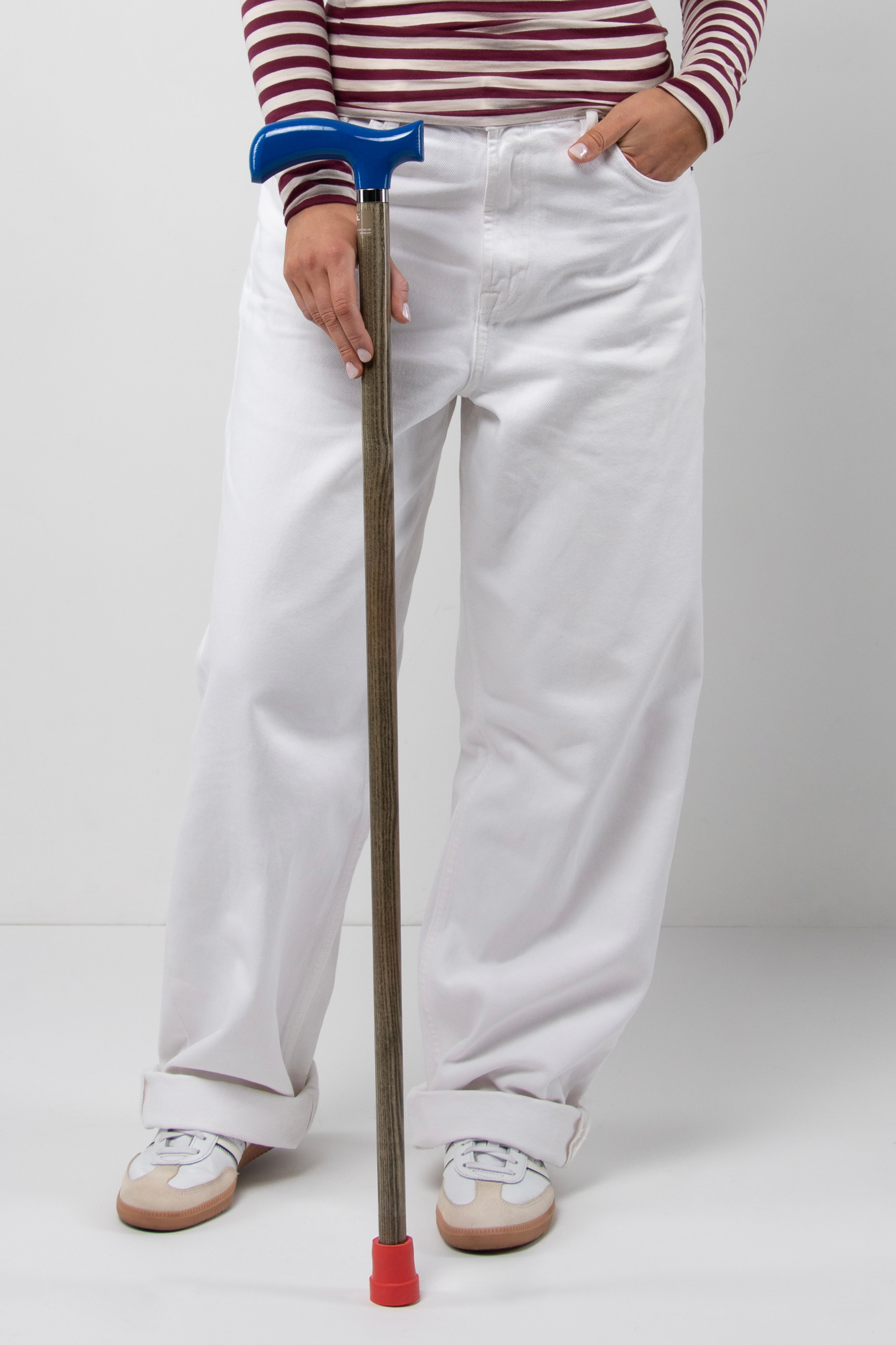 Young woman's walking cane with deep blue anatomical handle on light oak wood shaft. Sleek custom mobility aid for stable and silent support.