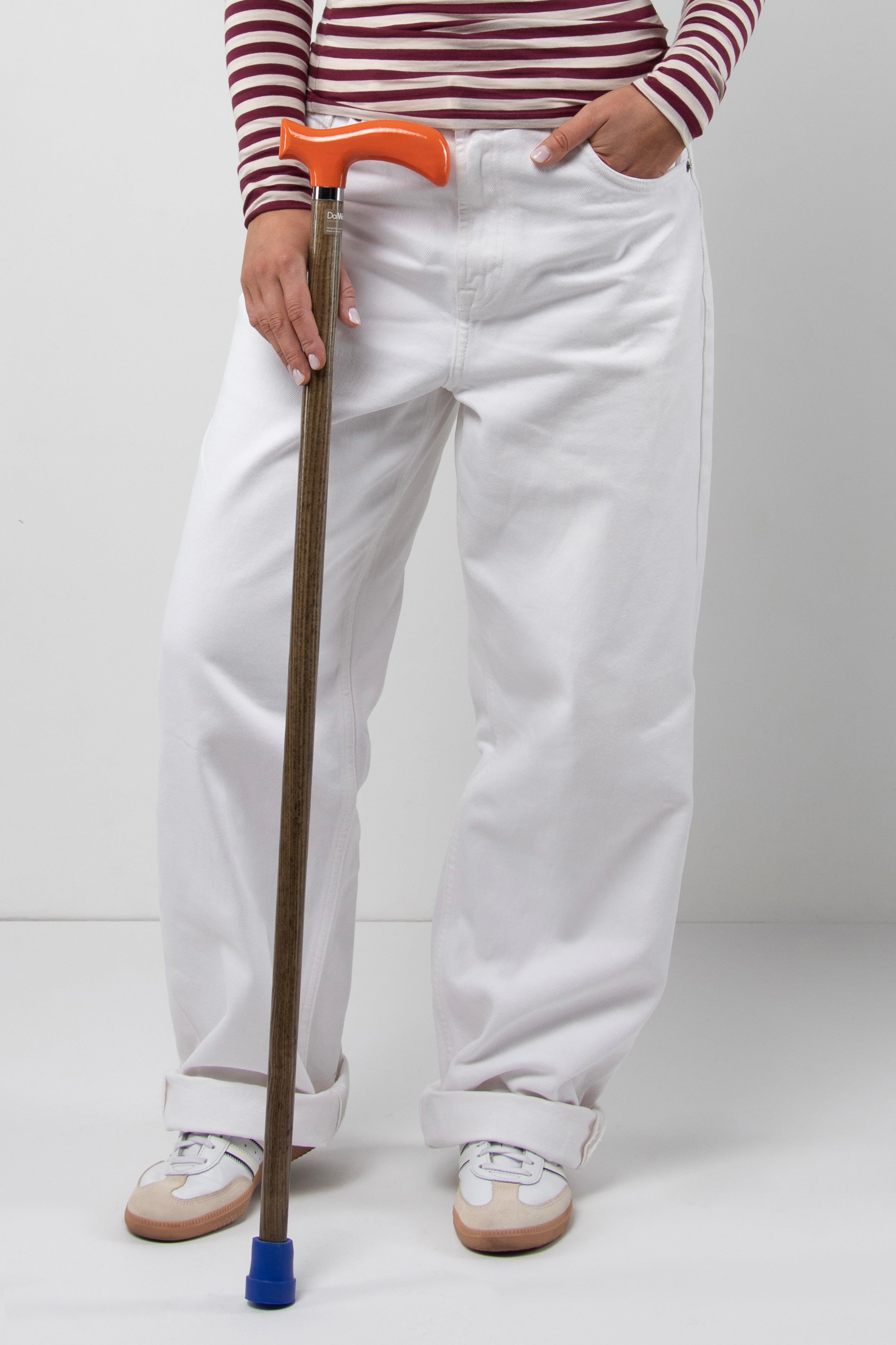 Lifestyle photo of a young woman with the DaiWalk Original 1.0 vibrant orange handle walking cane with oak wood shaft. Custom length anatomical grip mobility aid for women's perfect posture.
